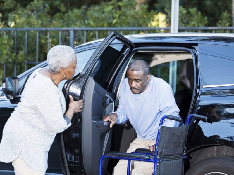 A man and woman with wheelchair access getting into a car provided by wheelchair transportation services.